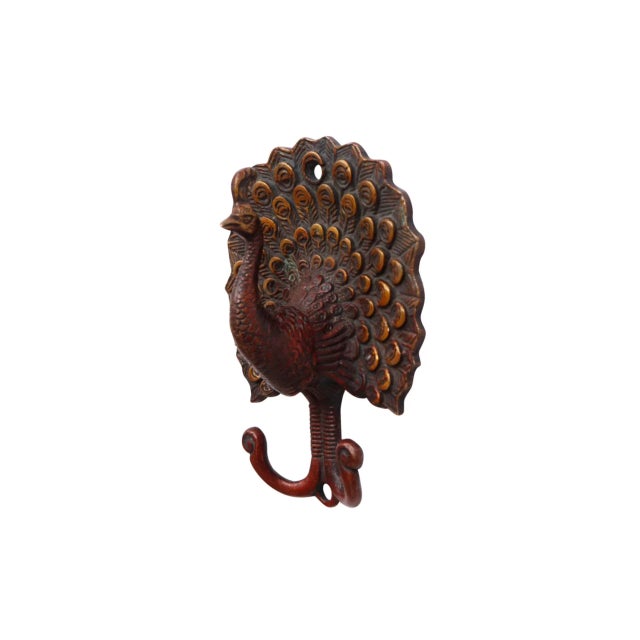 A dark red brass wall fixture with two hooks cast in the shape of a peacock. The backplate is shaped like a spread peacock...