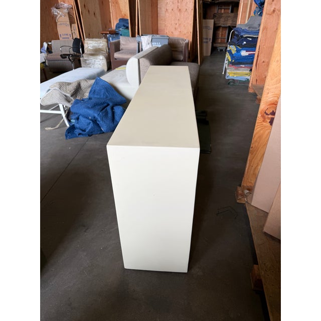 A striking sculptural console featuring a clean, architectural form finished in warm ivory lacquer, contrasted by an...