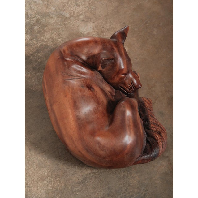 A beautifully hand-carved wooden sculpture depicting a dog curled peacefully in a resting position. The figure is sculpted...