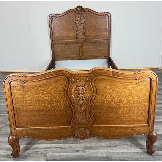 This Vintage French Louis single bed frame displays elegant carved detailing, flowing contours, and a warm oak wood finish...