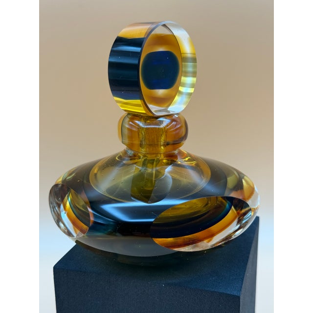 A striking vintage art glass perfume bottle featuring a sculptural, low-profile silhouette and a dramatic circular...