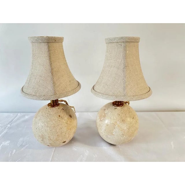 Pair of Travertine Novona Ball Table Lamps, with Brass Sockets, Silk wired cable, pivoting on a Brass Ring base. Ball is...
