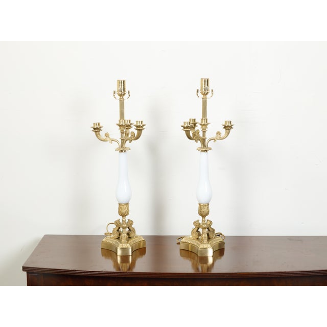 A pair of French Empire style bronze and opaline glass candelabra table lamps from the early 20th century, with scrolling...