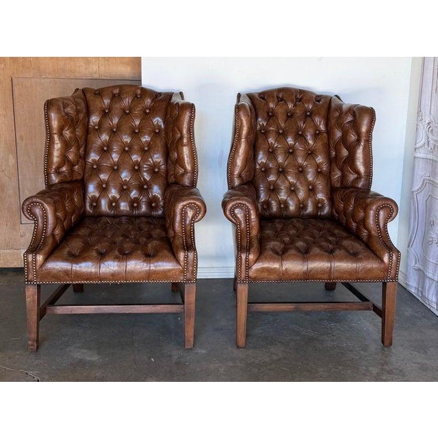 An exceptional pair of English Georgian-style wingback armchairs, embodying timeless British club sophistication and...