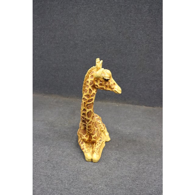 Decorative seated giraffe sculpture featuring a hand-painted finish with textured patterning and expressive facial...