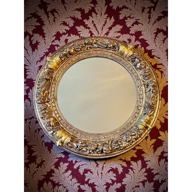 Impressive round gilt wall mirror featuring deeply sculpted fruit and ribbon garland detailing in a classical Florentine...