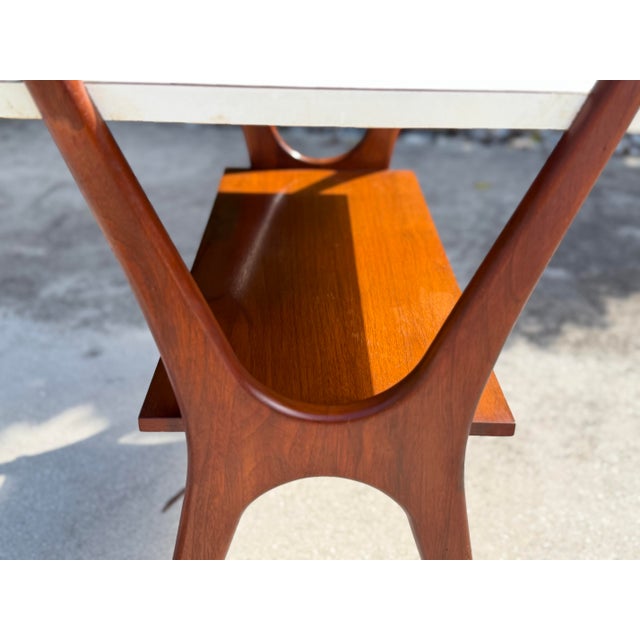 A distinctive mid-20th-century modern side table featuring a sculptural wood frame with elegantly curved side supports,...