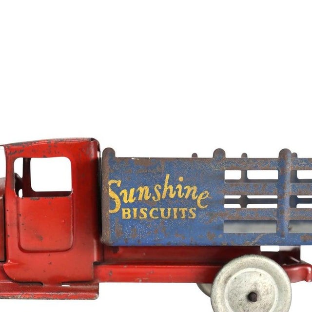 An antique pressed steel toy truck, dating to approximately 1920. This advertising vehicle features a vibrant red cab and...
