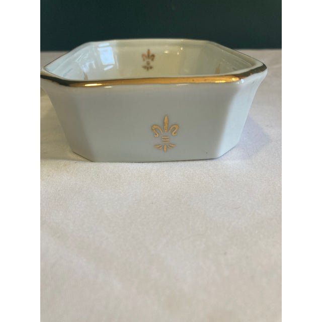 This elegant porcelain set includes a tapered cup and a small octagonal soap dish, both adorned with delicate gold fleur-...