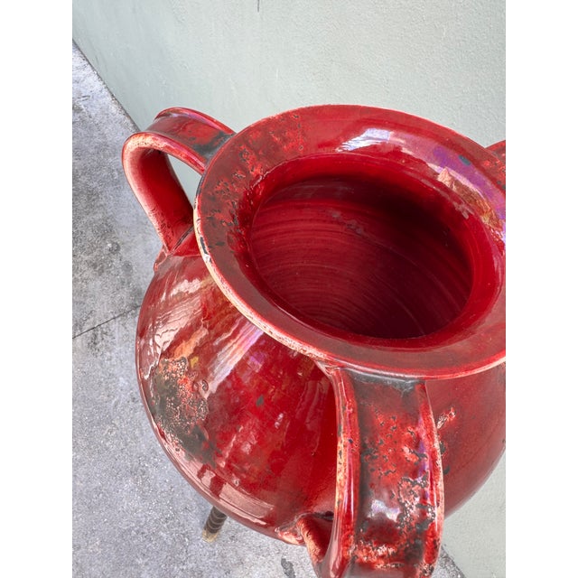 A bold double-handled ceramic jug in deep oxblood and crimson — the glaze pooling in volcanic rivulets toward the base....