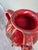 A bold double-handled ceramic jug in deep oxblood and crimson — the glaze pooling in volcanic rivulets toward the base....