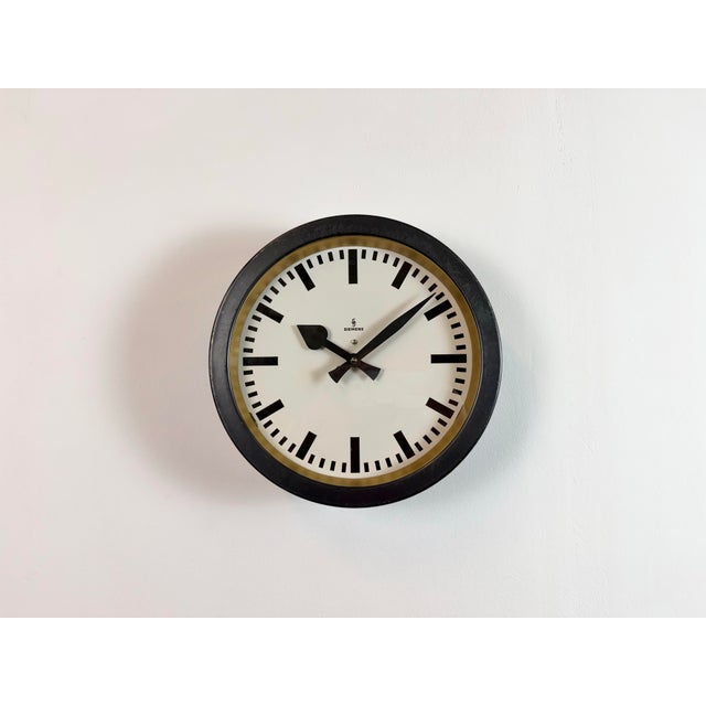 This wall clock was produced by Siemens in Germany during the 1950s. It features a black metal frame, a metal dial and a...