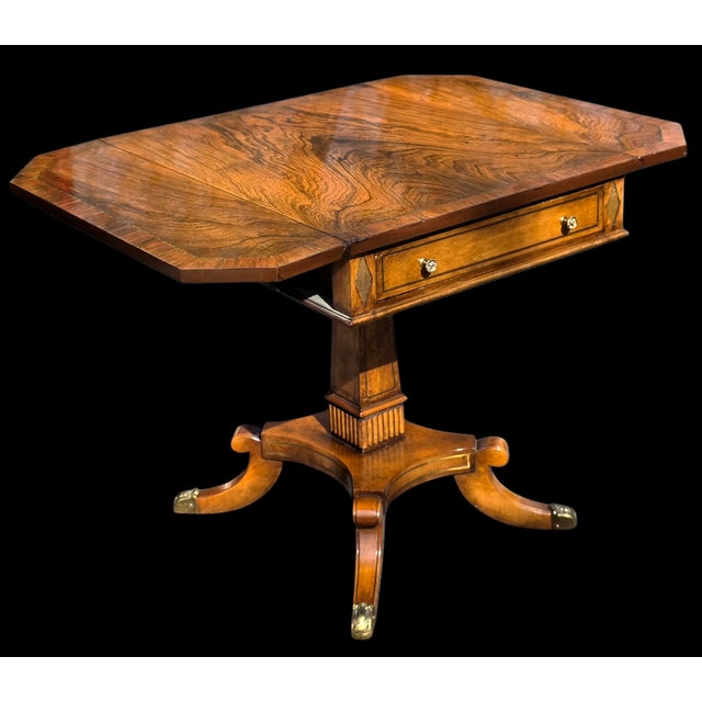 This Vintage Regency Revival Rosewood Pedestal Drop-Leaf Table with Drawer and Brass-Mounted Base is a highly decorative...