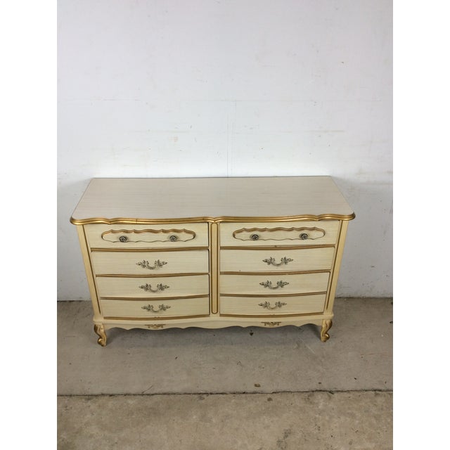 This mid century French Provincial style lowboy dresser features painted white finish, ornate brass hardware, and sculpted...