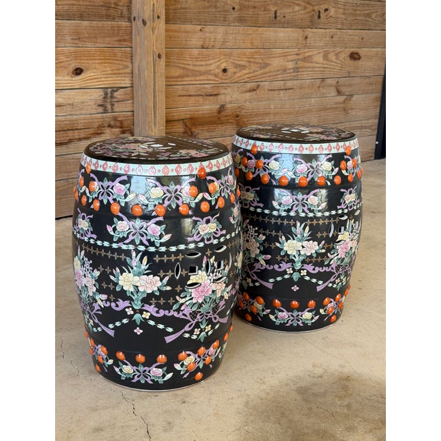A striking pair of Chinese export porcelain garden stools featuring a rich black ground with vibrant famille rose floral...