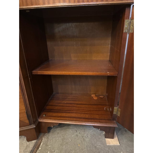 Elegant mid-20th-century Georgian-style mahogany breakfront china cabinet featuring classic dentil molding, flame mahogany...