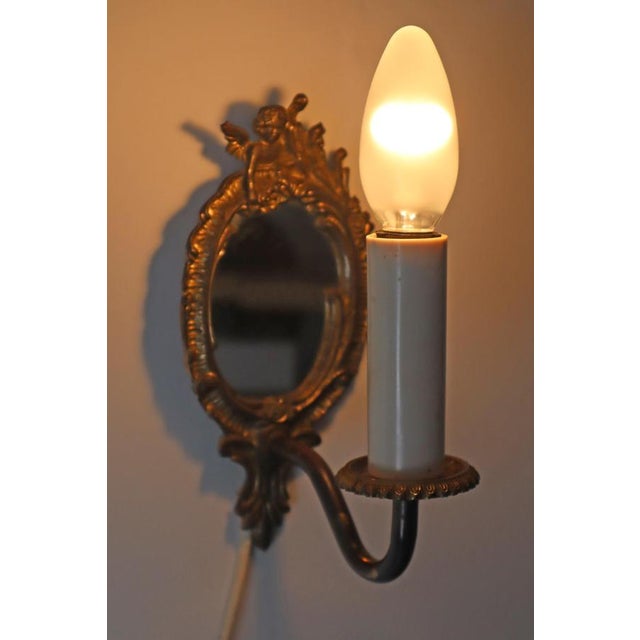 It is a set of two wall lamps, each with an angel on the top. Both lamps have mirrors. The lamps are gold plated. The...