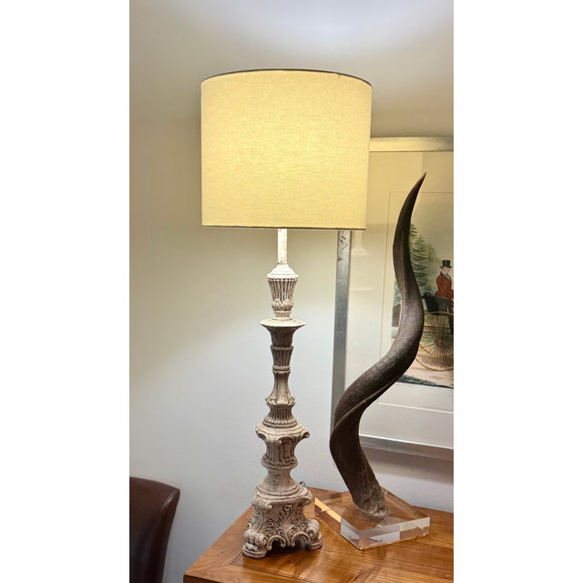Ornate candlestick-style table lamp with carved scroll and leaf details on a footed base. More than likely, this was...