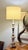 Ornate candlestick-style table lamp with carved scroll and leaf details on a footed base. More than likely, this was...