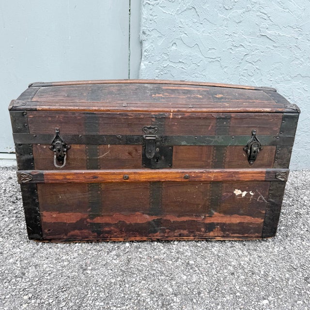 A striking late 19th-century wooden steamer trunk featuring a gently curved barrel top, dark iron banding, decorative...