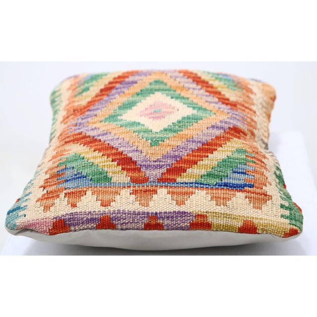 A one-of-a-kind handwoven Afghan wool kilim lumbar pillow featuring concentric stepped diamonds in green, purple, red and...