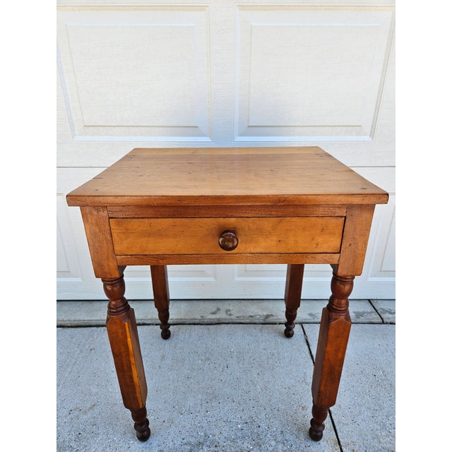A classic antique primitive side table with one drawer and turned legs. This piece is in good antique condition with age-...