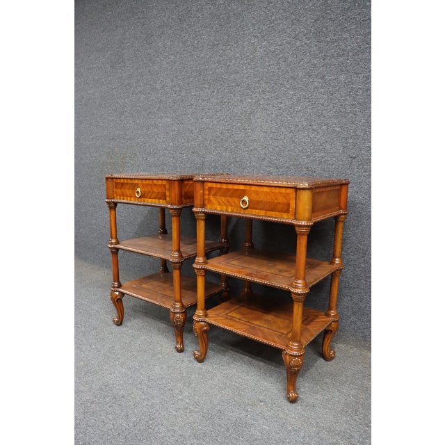 Pair of Maitland-Smith mahogany nightstands with inlaid tops and shelves. Each table features one drawer with a brass ring...