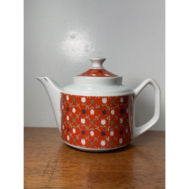 Charming vintage porcelain teapot featuring a red and white floral pattern with classic mid-century styling. Elegant...
