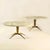 Pair of oval coffee tables with Carrara marble top supported by a sculpted cast brass base with a relief of figures is...