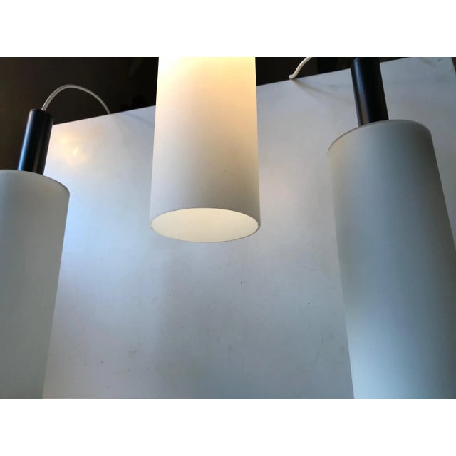 A trio of 'hammer' or 'mallet' shaped pendant lamps composed of matté cased opaline glass and top made from powder coated...