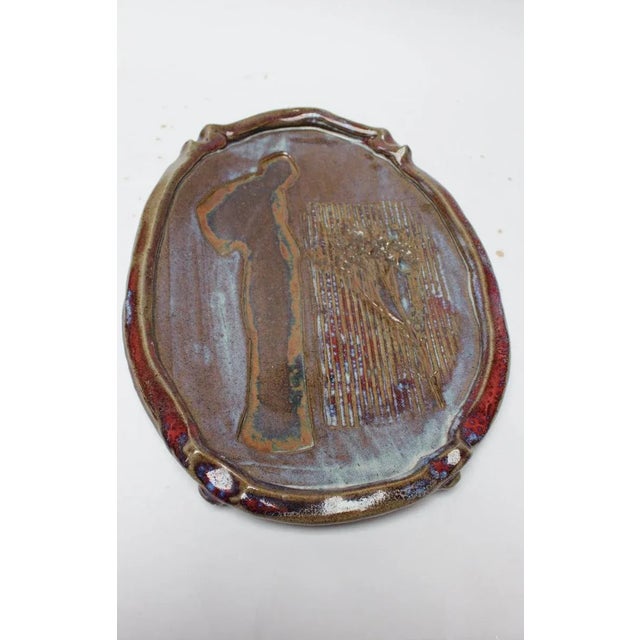 Figural charger by ceramicist, Pollack depicting a man gazing at a growing tree (USA, 1977). Attractive color combinations...