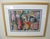 Framed watercolor painting featuring an assemblage of colorful, stylized tribal, ceremonial, and everyday masks with...