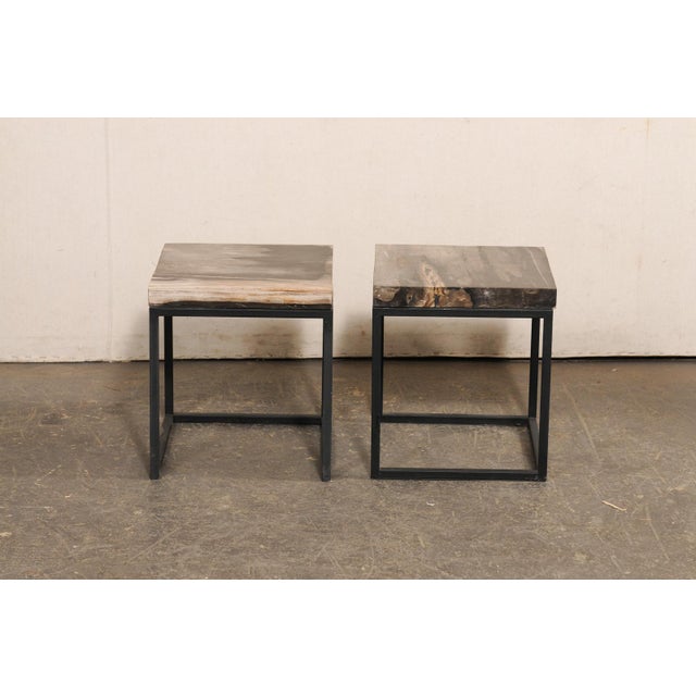 A pair of modern style, custom created petrified wood top and iron side tables. This pair of tables each feature a square-...