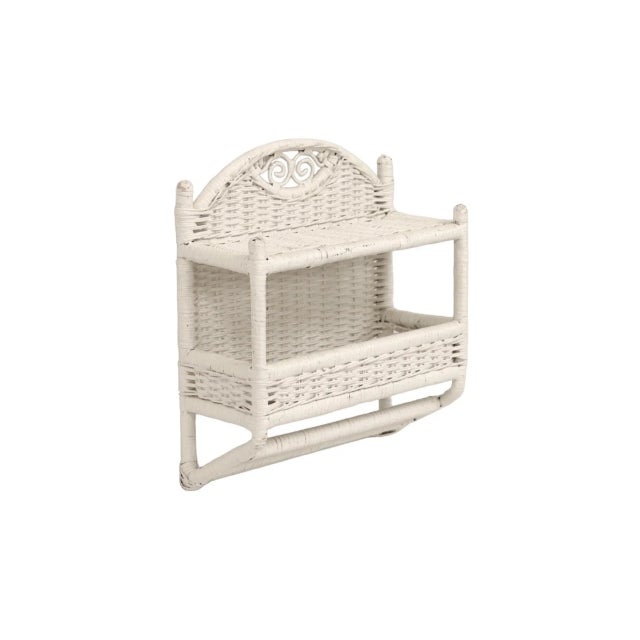 A white bamboo and wicker wall shelf unit. A bamboo frame supports two wicker shelves secured with rattan. Shelves are...