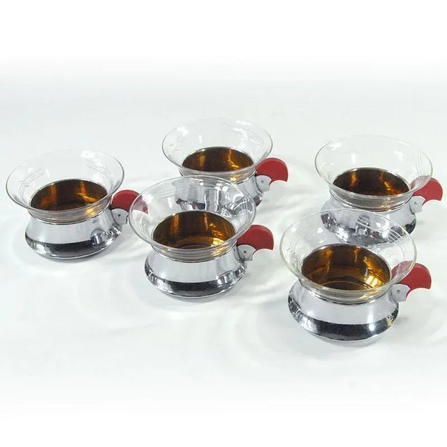 A set of six glasses in a metal, chrome basket, inside in golden color. The handles are made of dark red bakelite dyed....