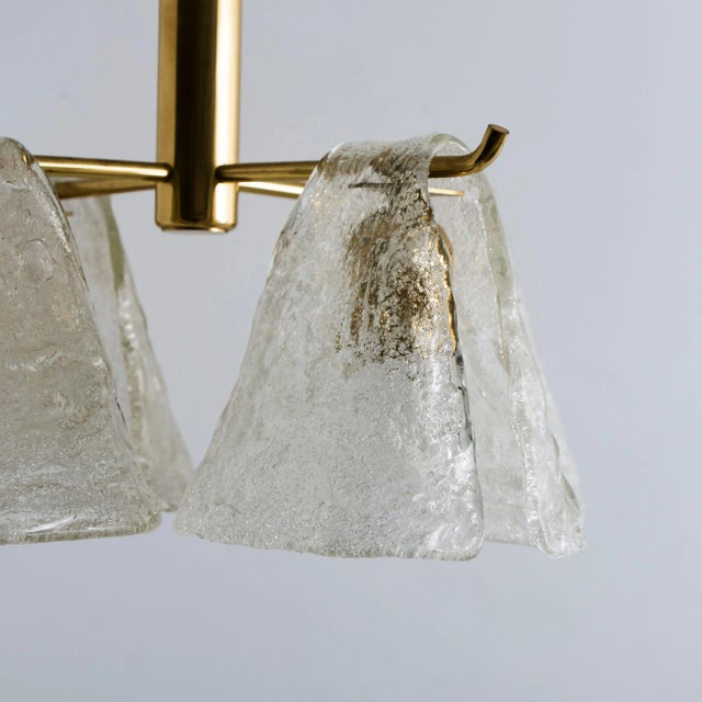 This chandelier features a brass structure over which four blown glass lampshades seem to be pouring over. Illuminates...