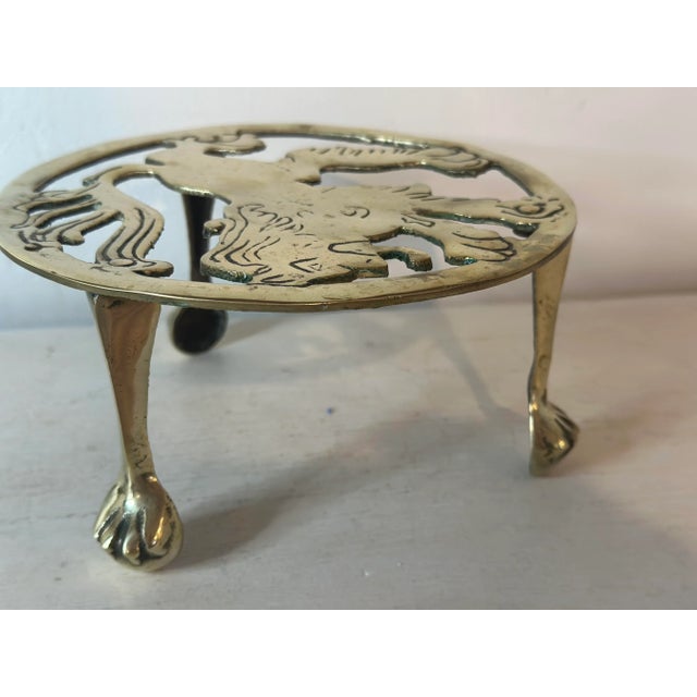 A finely crafted vintage English brass trivet, its design distinguished by graceful legs terminating in paw-shaped feet—a...