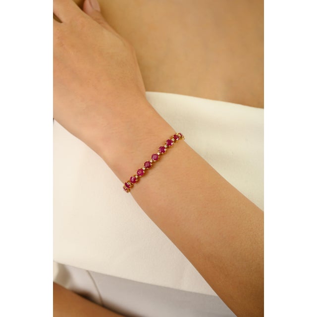 This delicate tennis bracelet showcases 30 round-cut rubies totaling 12.99 carats, set in luxurious 18K yellow gold. Each...