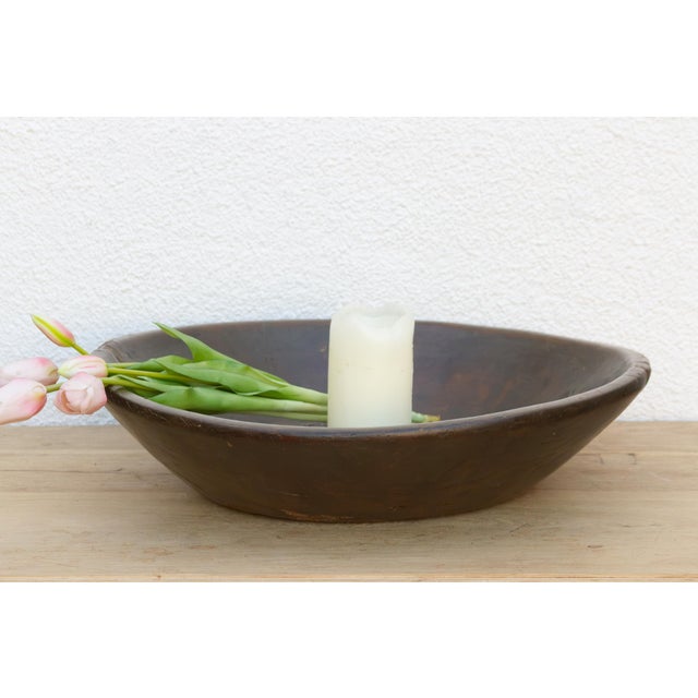 A broad, shallow bowl of dark wood curves up to a thick, softly rounded rim, its surface darkened to a deep oxidized brown...