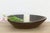 A broad, shallow bowl of dark wood curves up to a thick, softly rounded rim, its surface darkened to a deep oxidized brown...