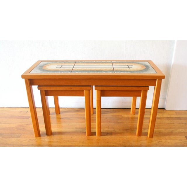 This is a mid century modern set of 3 Danish teak nesting tables. Each table has a teak frame and a tile top with a...