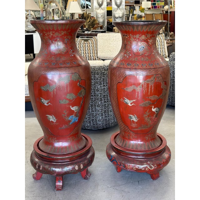 A pair of monumental red lacquered Chinese palace vases on stands. These are crafted out of wood and paper mache. There...