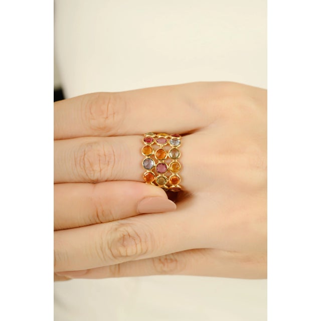 This vibrant wide band ring features 10.1 carats of round-cut rainbow sapphires, expertly set in a 14K yellow gold bezel...