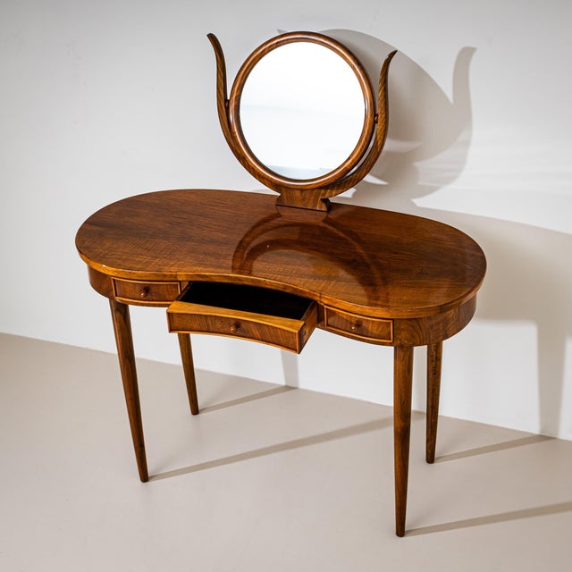 Vanity table crafted from solid walnut, featuring a kidney-shaped top with three drawers and raised on tall, tapering...