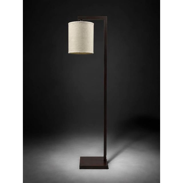 A modern minimalist floor lamp with a clean rectangular frame, square base, and cream fabric drum shade. The frame...