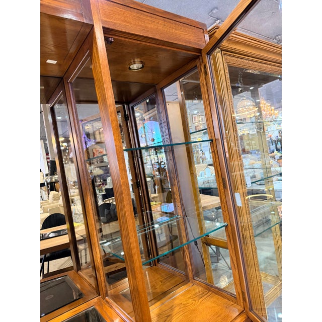 A vintage Thomasville oak wall unit cabinet featuring glass-front display towers on each side and a mirrored center...