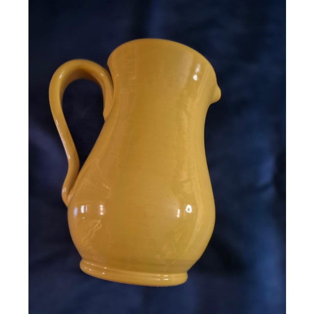 This hand-crafted Italian ceramic pitcher features a classic bulbous silhouette with a vibrant ochre yellow glaze and a...