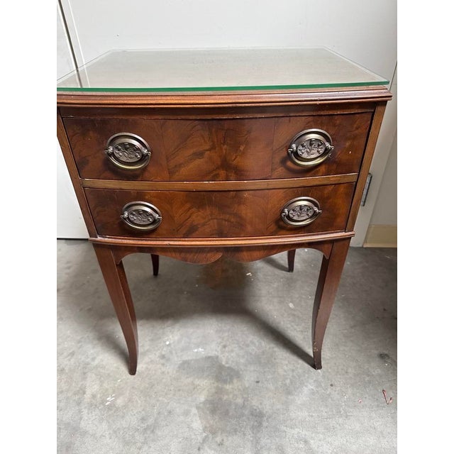 Elegant vintage two-drawer nightstand featuring beautifully figured wood grain, a warm reddish-brown finish, and classic...