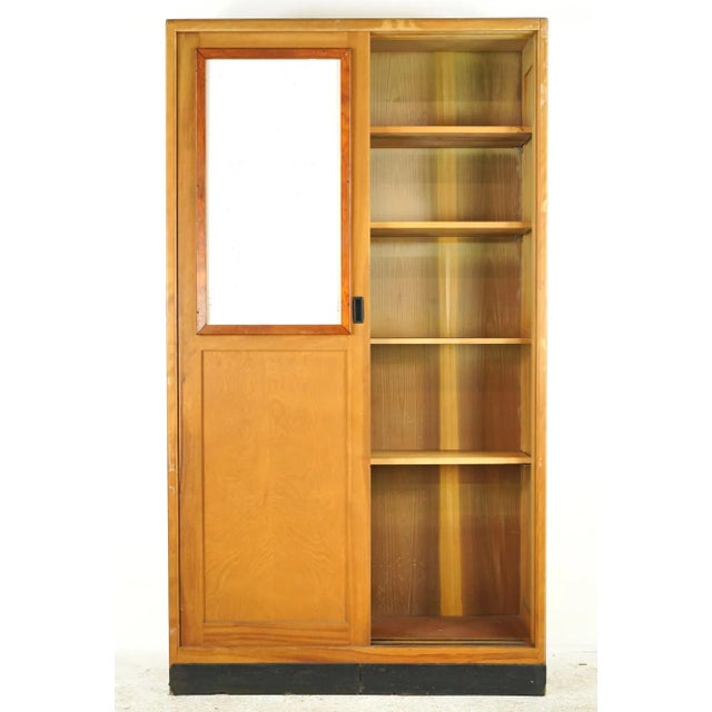 Reclaimed built-in storage cabinet in a medium wood tone stain, two sliding doors, and a black rubber toe kick. It...