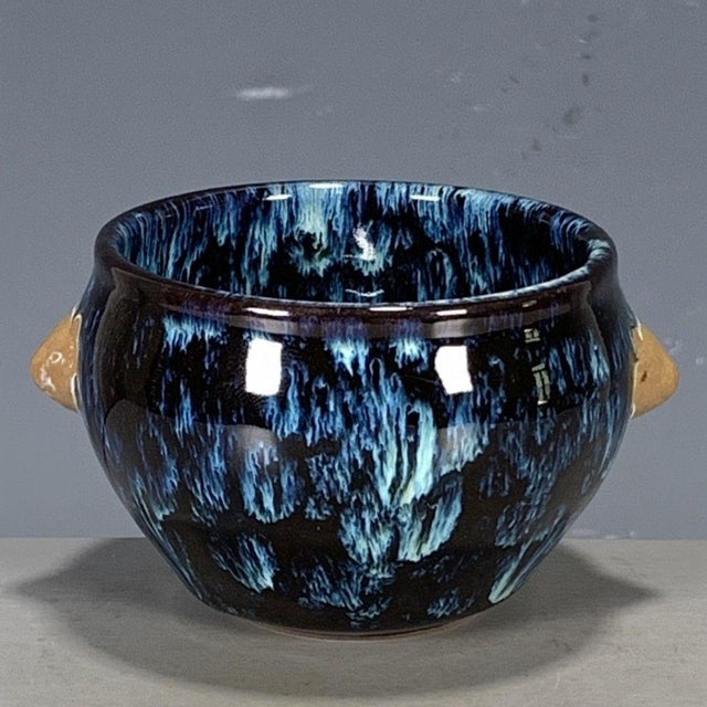 This is a striking vintage porcelain teacup, featuring a dramatic flambé glaze and applied beast-head handles. The cup is...